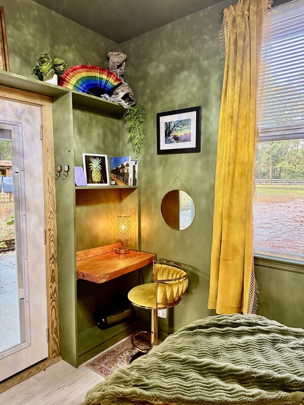 A room with a green wall, a wooden desk, a yellow chair, a mirror, and a window with yellow curtains.