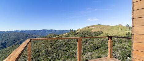 A wooden deck with a metal railing overlooking a hilly landscape with distant mountains.