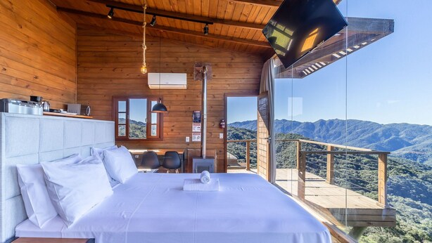 Un dormitorio con una cama grande, techo de madera, televisor y vistas a la montaña.