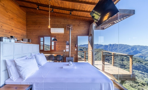 Camera da letto con un ampio letto, soffitto in legno, televisione e vista sulle montagne.