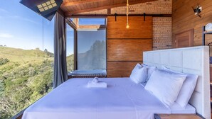 Une chambre avec un grand lit, une vue sur un paysage vallonné, des murs en bois et un design moderne au niveau du plafond.