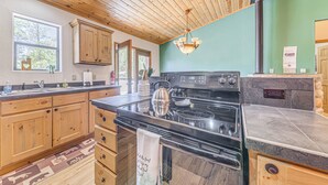 Une cuisine avec des meubles de rangement en bois, un poêle noir et un mur vert.