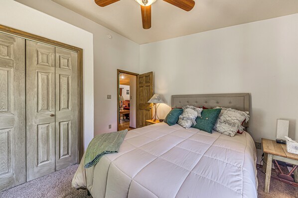 A bedroom with a large bed, a wooden wardrobe, a ceiling fan, and a bedside table with a lamp. - < 2 Mi to Midtown Ruidoso: Forest-View Sanctuary! (Ruidoso)