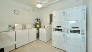 A laundry room with multiple washing machines, a clock, and a ceiling fan. - Estero Beach & Tennis 1001-a (Fort Myers Beach)