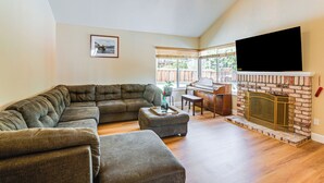 Una sala de estar con sofá modular, reposapiés, chimenea, piano y televisor.