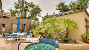 A swimming pool with a blue tiled edge, surrounded by palm trees and a patio area with blue chairs and a table. - Near Golf & Trails! Pet-Friendly Scottsdale Condo (Scottsdale)