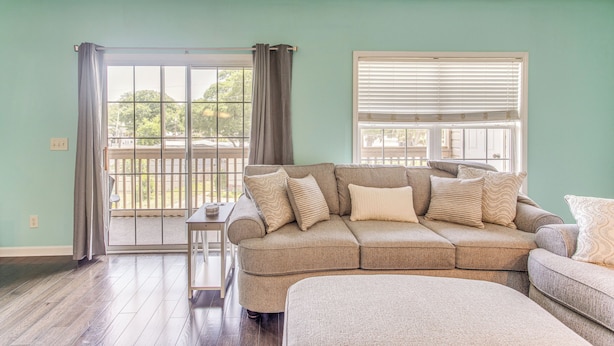 A living room with a sectional sofa, a small side table, and a view through a sliding glass door to the outside. - 1 Mi to Beach, Near Golf! North Myrtle Beach Condo (North Myrtle Beach)