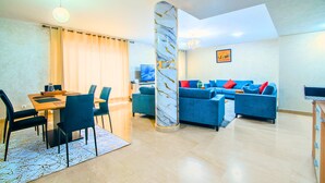 A modern living room with a dining area, a large blue sofa set, a marble pillar, and a chandelier. - Agadir Bay Beautiful apartment overlooking the pool and nearby beach. (Agadir)