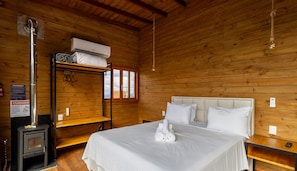 Habitación de cabaña de madera con literas, un calentador, una cama con ropa blanca y vista al exterior por una ventana.