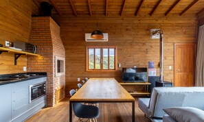 Interior acogedor de una cabaña con detalles de madera, una chimenea de ladrillo, una mesa de comedor y un televisor.