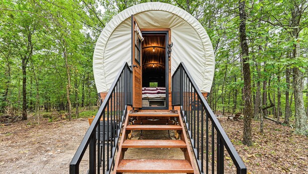 Una tienda de campaña con una escalera de madera que lleva a una cama en su interior, rodeada por un bosque.