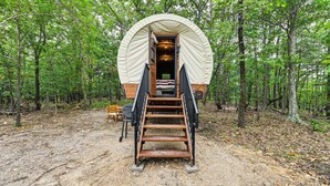 Una estructura de madera cubierta con una escalera que conduce a una entrada, rodeada por un bosque.