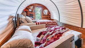 Un acogedor espacio tipo tienda con forma circular, que incluye una cama, almohadas, una colcha, una pared de madera con un espejo y un cartel.
