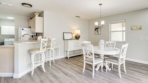 A modern kitchen with white cabinetry, a central island, and a dining area with white chairs and a round table. - 6 Mi to Lake Sumter Landing: Home w/ Perks! (The Villages)