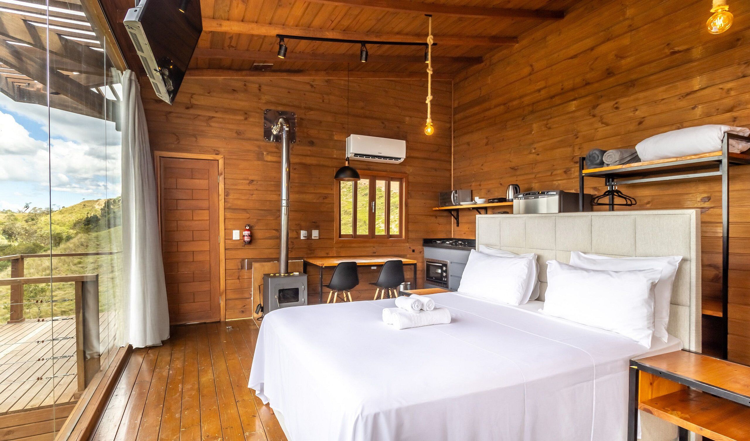 Quarto de cabana de madeira com uma cama, uma escrivaninha, uma cadeira e vista para o exterior.