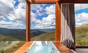 Une terrasse en bois avec un jacuzzi donnant sur un paysage montagneux.