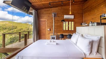 Un dormitorio con una cama grande, techo de madera, ventana con vistas al campo y una pequeña mesa con sillas.