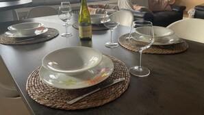 Mesa de comedor dispuesta con platos, vasos y una botella de vino, con vista a edificios a través de la ventana.