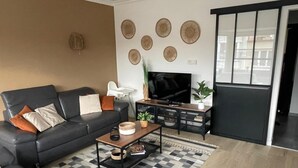Una sala de estar moderna con un sofá de cuero negro, una mesa de centro, un televisor sobre un mueble bajo y platos decorativos en la pared.