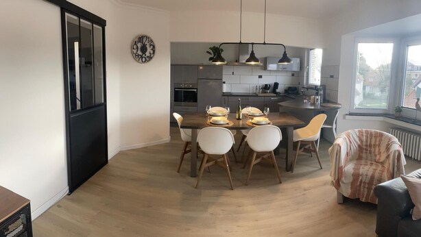 Una cocina moderna con comedor, que incluye una isla central, iluminación colgante y vistas al exterior.
