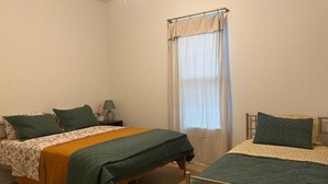 Un dormitorio con dos camas, una ventana con cortinas y una mesita de noche con lámpara.