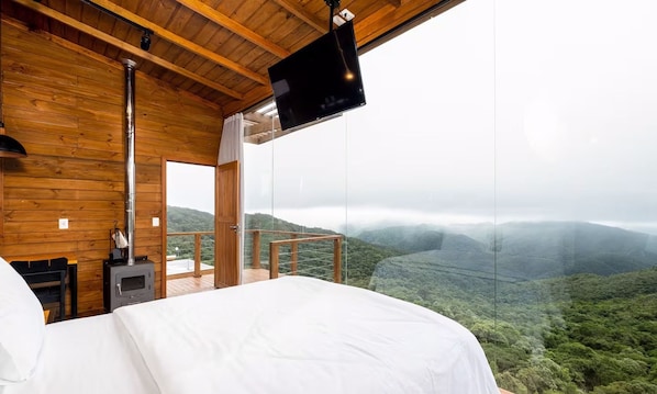A bedroom with a bed, a TV, and a view of a mountainous landscape.