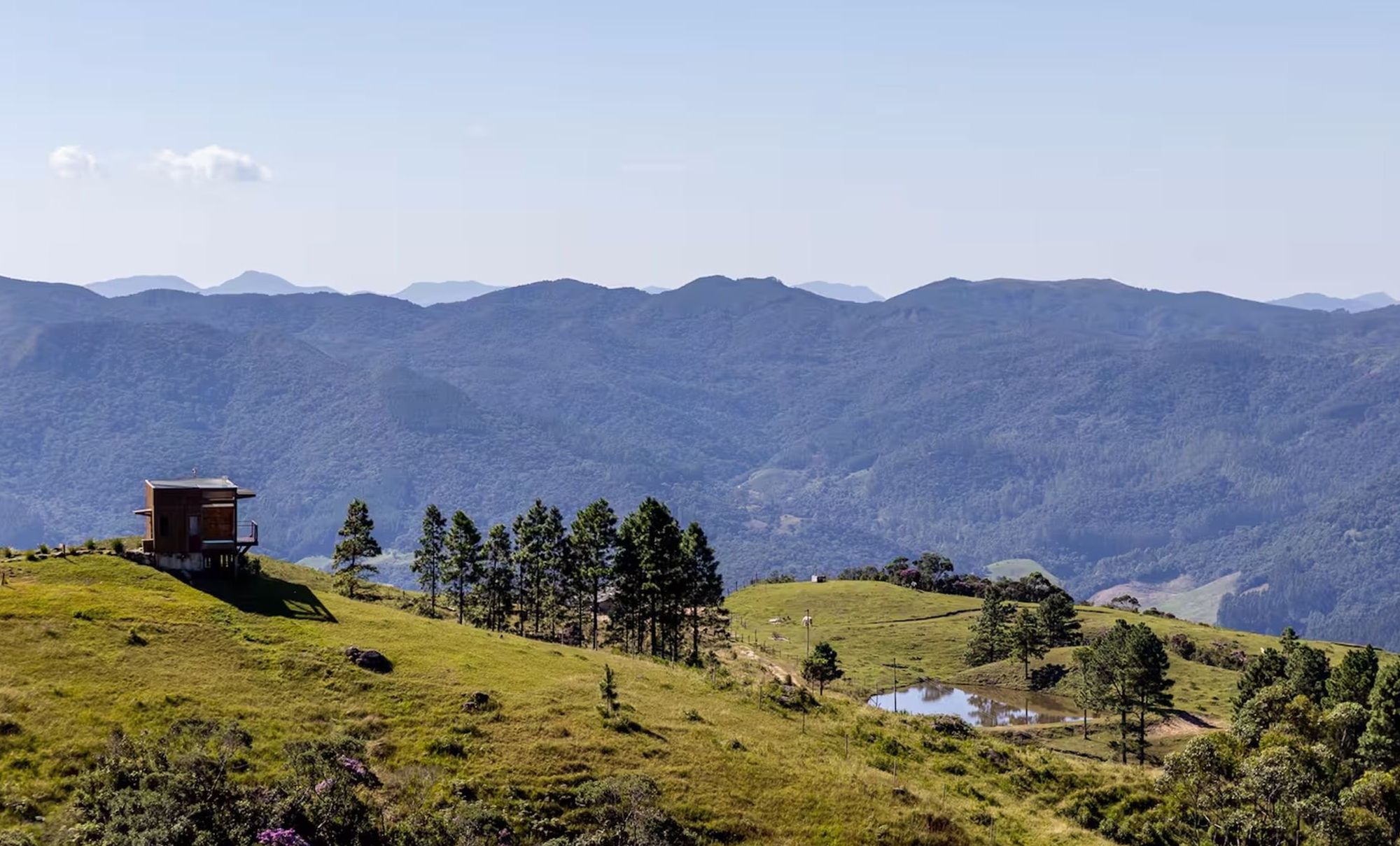 A mountain landscape with a small wooden cabin on a grassy hill.