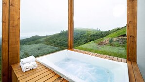 Une terrasse en bois avec un jacuzzi et des serviettes, offrant une vue sur un paysage verdoyant.