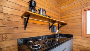 Une cuisine avec des murs en bois, une cuisinière à gaz, une machine à café et une bouilloire posée sur une étagère.