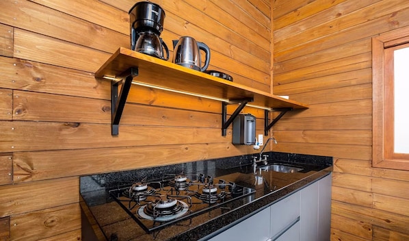 A kitchen with wooden walls, a gas stove, a coffee maker, and a kettle on a shelf.