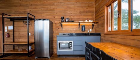 Una cocina compacta con paredes de madera, un refrigerador de acero inoxidable, un horno empotrado y una mesa de comedor de madera con sillas.