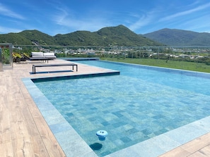 A swimming pool with clear blue water, surrounded by a wooden deck and a lounge area with white chairs. - Studio Shopping OKA Floripa - SOK218 (Florianopolis)