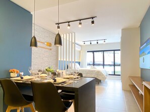 A modern hotel room with a dining area, a bed, and large windows.