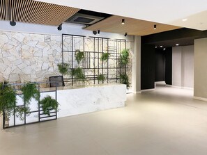 A modern lobby with a stone wall, a reception desk, and a staircase.