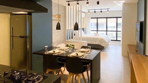 Una cocina moderna con comedor, un ventanal grande y un dormitorio con cama y televisor.