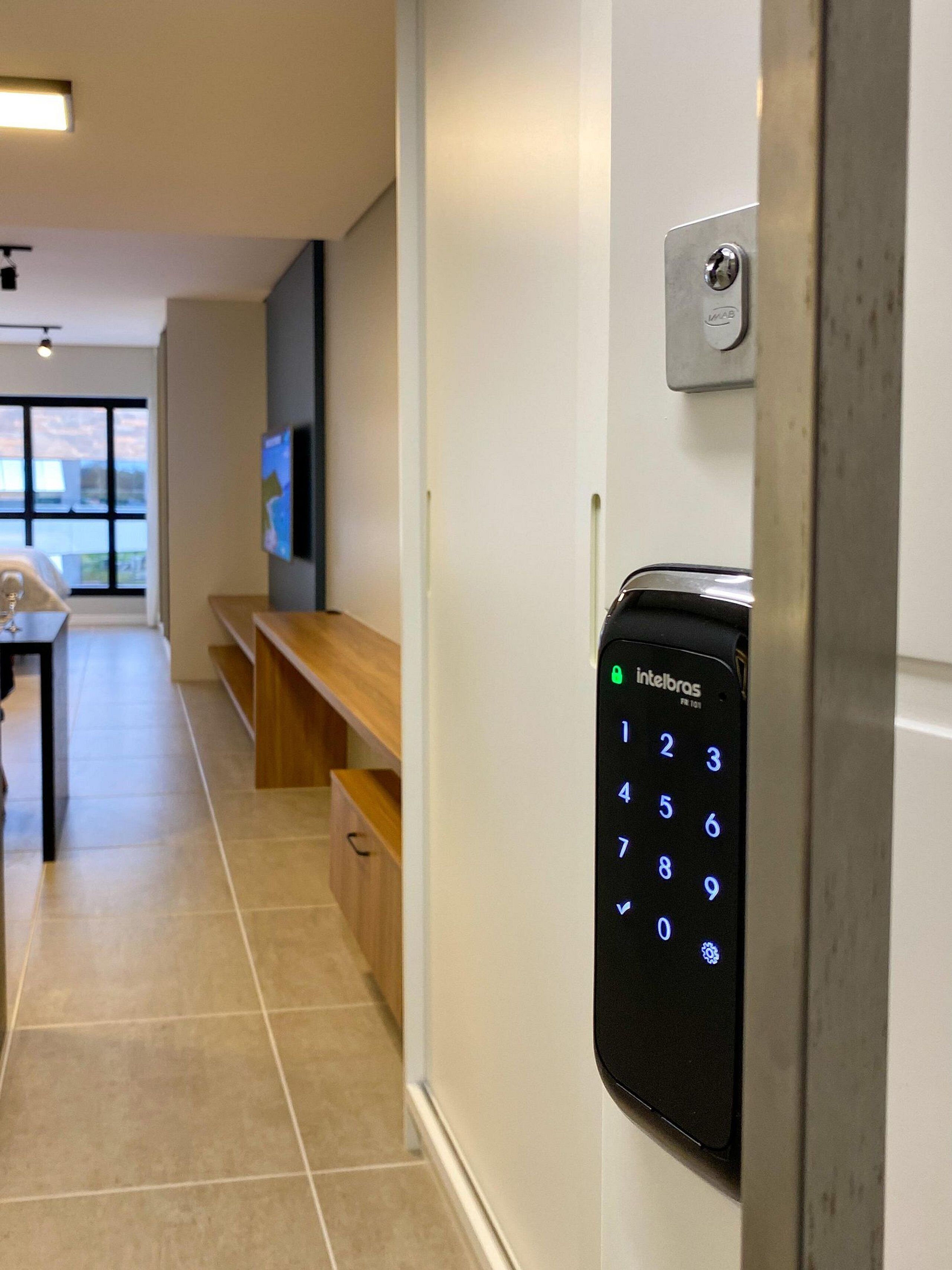 Un couloir avec une porte à code, un banc, une table avec un verre à vin et un téléviseur fixé au mur.