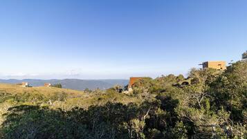 Un paysage avec des bâtiments situés sur une colline, entourés d’arbres et avec des montagnes visibles au loin.