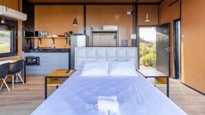 A modern bedroom with a large bed, a small kitchenette, and a view of the outdoors. - Cabana jacuzzi e vista montanhas VST031 (Anitápolis)