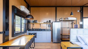 A compact kitchen with a dining area, a refrigerator, and a hanging light fixture. - Cabana jacuzzi e vista montanhas VST031 (Anitápolis)