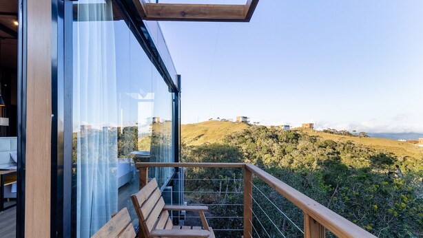 A wooden deck with a bench, overlooking a hilly landscape with buildings in the distance. - Cabana jacuzzi e vista montanhas VST031 (Anitápolis)
