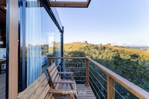 A wooden deck with a bench, overlooking a hilly landscape with buildings in the distance.