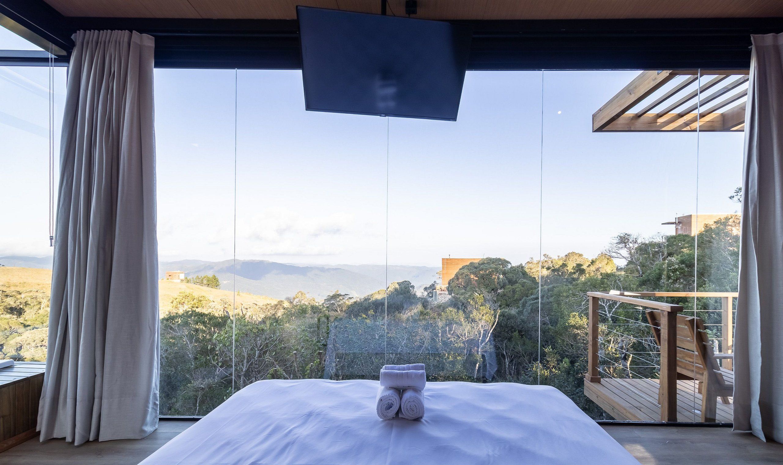 Een slaapkamer met een bed, een televisie en een balkon met uitzicht op het landschap.