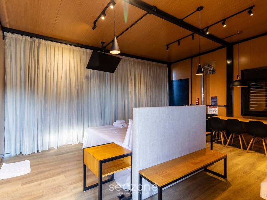 A hotel room with a bed, a desk, a bench, and a dining area with chairs.