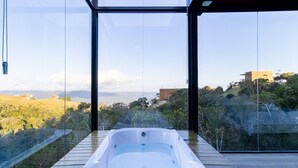 Un bain à remous extérieur moderne offrant une vue dégagée sur un paysage vallonné et des bâtiments situés au loin.