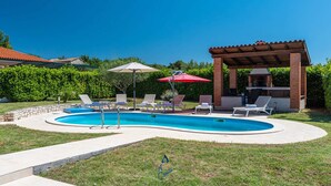 A swimming pool with lounge chairs and umbrellas, a brick barbecue area, and a clear blue sky. - Charming 2-Bedroom Villa with private heatable pool (Višnjan)