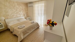 Une chambre à coucher avec un lit, des tables de chevet, une commode, une fenêtre avec des rideaux et un vase rempli de fleurs sur une table de chevet.
