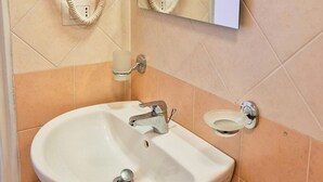 Une salle de bain avec un lavabo sur colonne, un miroir et un sèche-cheveux fixé au mur.