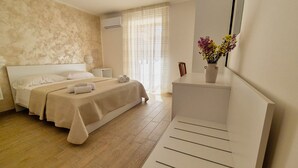 Une chambre à coucher avec un lit, des tables de chevet, une commode, un miroir et une fenêtre avec des rideaux.