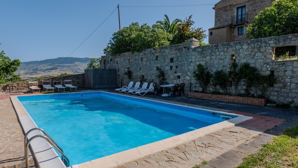 Une piscine rectangulaire avec un mur en pierre et un bâtiment en pierre en arrière-plan.