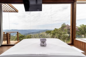 A bedroom with a large bed, a wooden deck, and a scenic view of mountains and trees. - Cabana Vista Serra em Anitápolis VST032 (Anitapolis)